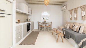 Una cocina compacta con armarios blancos, un comedor con mesa redonda y sillas, y un sofá con cojines estampados.