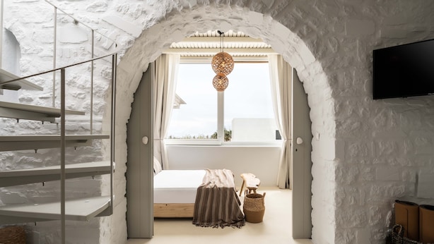 Un dormitorio con pared de ladrillo blanco, una cama, un televisor, una ventana con cortinas, una lámpara colgante y una escalera.