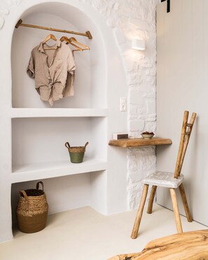 A room with a white brick wall, wooden shelves, a wooden chair, and a hanging rack with clothes.