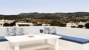 Una terraza con mesa blanca y cojines azules, con vistas a un paisaje montañoso con edificios.
