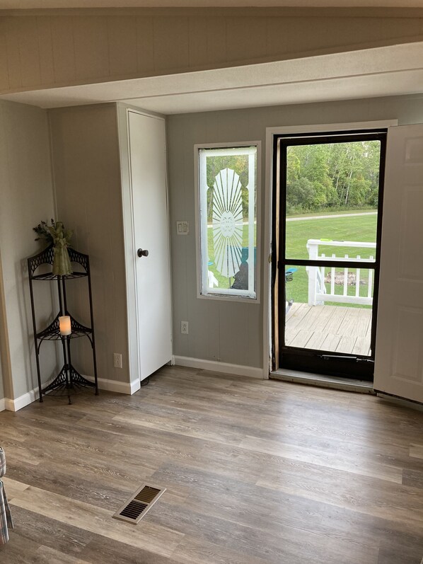 Ein Zimmer mit Holzboden, einer weißen Tür, einem Fenster mit dekorativer Glasverkleidung und Blick auf eine Terrasse und Grünfläche.
