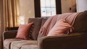 A cozy living room with a sofa, a knitted throw blanket, and a window with curtains.
