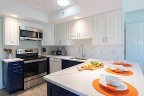 A modern kitchen with white cabinets, stainless steel appliances, and a breakfast setup on the island.