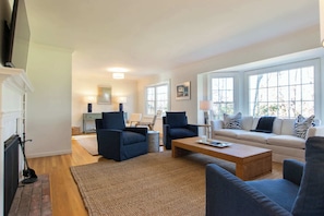 A living room with a fireplace, two armchairs, a sofa, a coffee table, and a large window with a view.