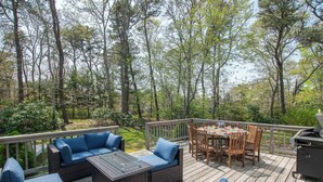A deck with outdoor furniture, including sofas and a dining table, surrounded by trees. - Gorgeous Home with Game Room Dog Welcome! (Chatham)