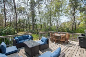 A deck with outdoor furniture, including sofas and a dining table, surrounded by trees. - Gorgeous Home with Game Room Dog Welcome! (Chatham)
