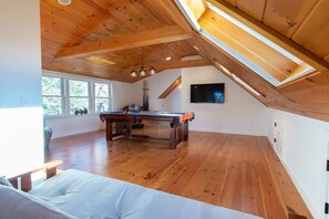 Een ruime kamer met een houten plafond, een pooltafel en een groot raam.