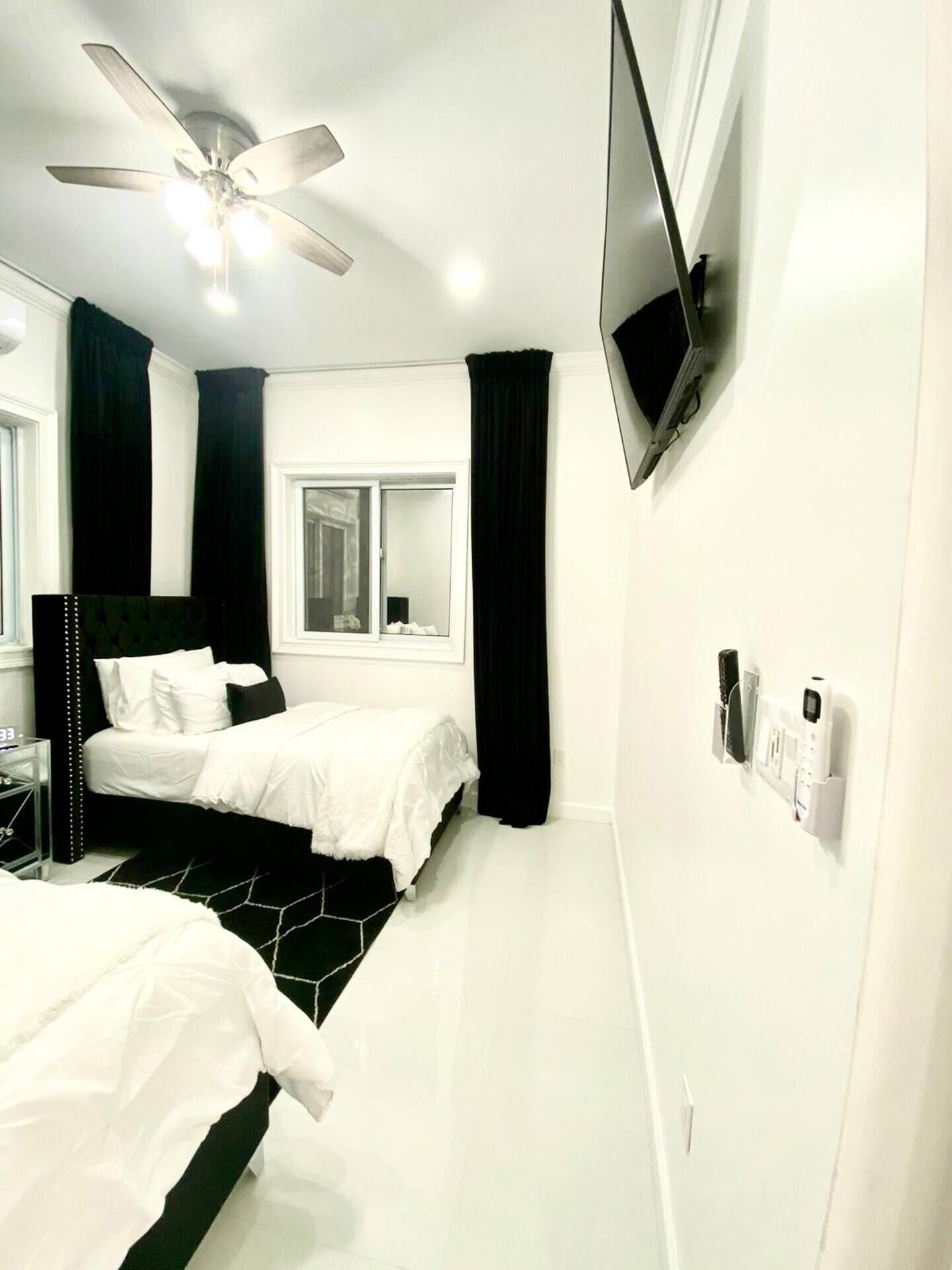 A modern bedroom with a bed, a ceiling fan, a TV mounted on the wall, and a window with curtains.