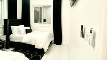 A modern bedroom with a bed, a ceiling fan, a TV mounted on the wall, and a window with curtains.