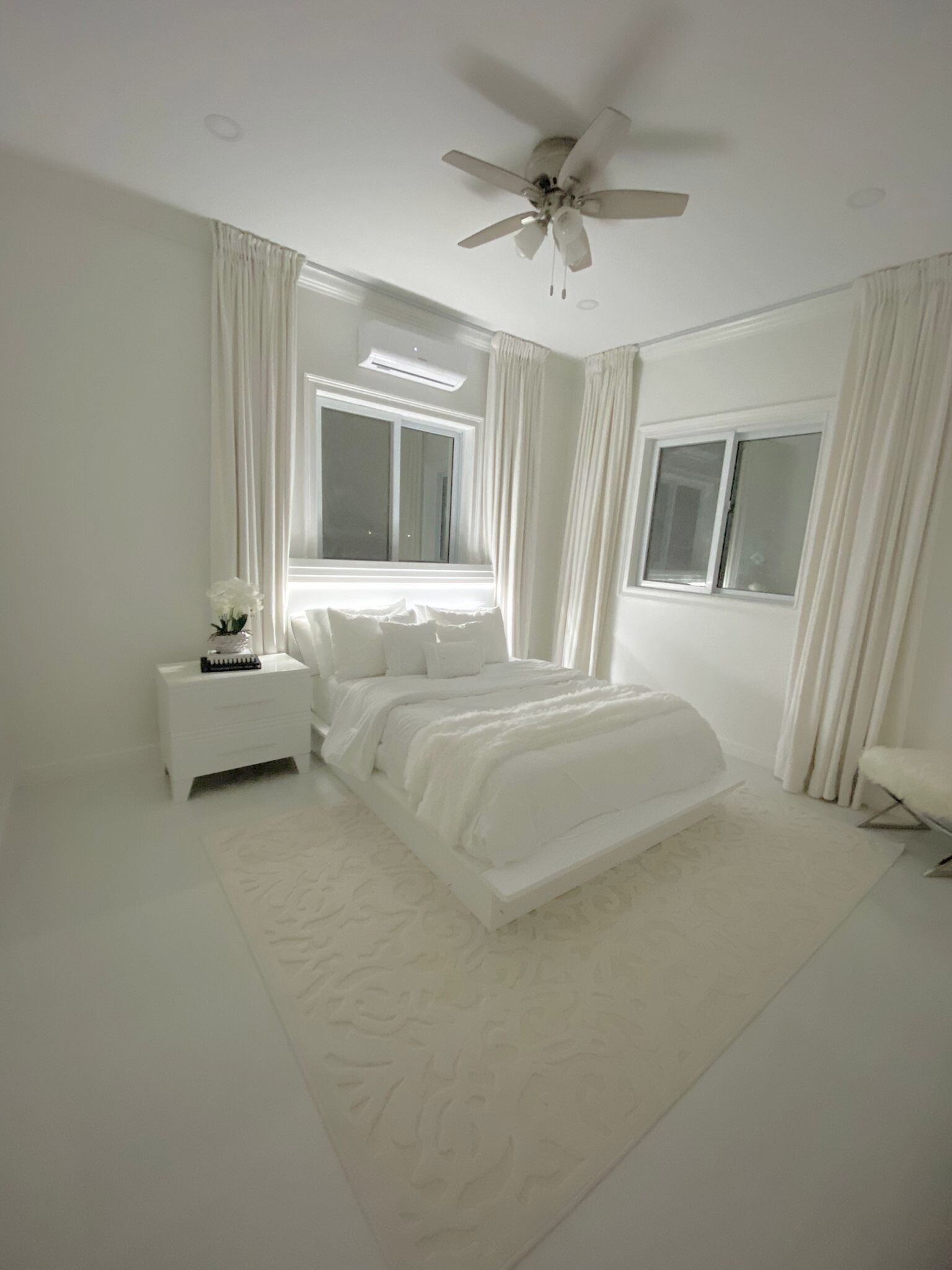 Une chambre à coucher avec un lit, une table de chevet, une fenêtre et un ventilateur de plafond.