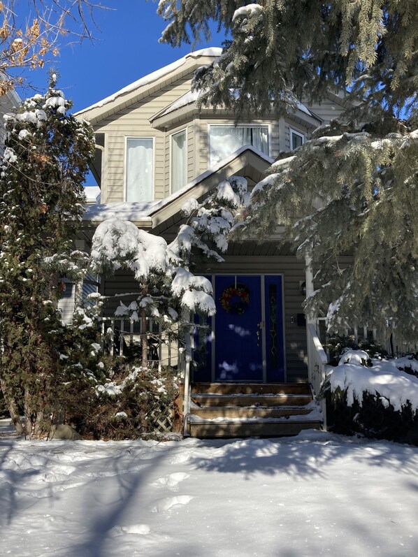 Uma casa com porta azul, árvores cobertas de neve e céu azul e límpido.