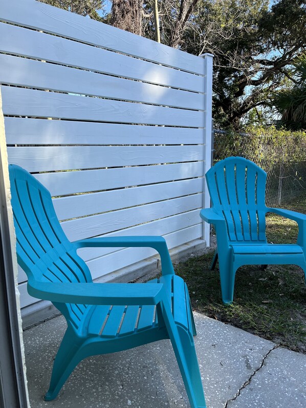 Two turquoise Adirondack chairs positioned on a concrete patio adjacent to a white wooden fence.