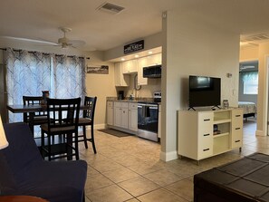 A compact living space with a dining area, kitchenette, and a TV on a stand.