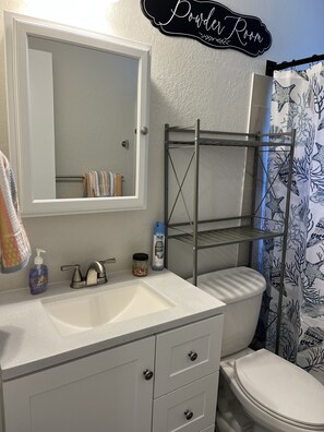 A bathroom with a white sink, a mirror, a toilet, and a shower curtain with a marine life pattern. There is a shelf above the sink and a towel hanging on the wall. -  ❤️❤️RIVERSIDE  RETREAT RIVERWALK,  PETS OK WITH FEE 🐕🐈 FISH ACROSS STRET🎣🐠 (Port Richey)
