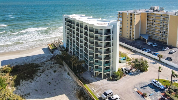 A beachfront hotel with multiple floors, a parking lot, and a view of the ocean.
