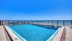 A rectangular swimming pool with a clear blue water, surrounded by a black metal fence, and a view of the ocean in the background.