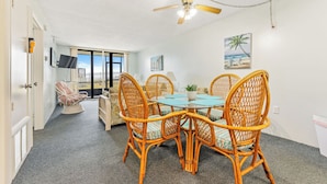 Un coin repas avec des chaises en osier et une table en verre, un ventilateur de plafond et une vue sur l’extérieur.