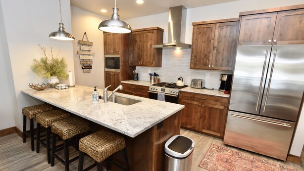 A kitchen with a central island, wooden cabinets, stainless steel appliances, and a trash can. - Silverpine Gem - Downtown - Walk to shops, restaurants, Payette Lake - WiFi (McCall)