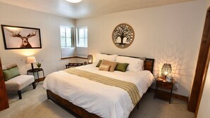 A bedroom with a large bed, a nightstand with a lamp, a bench, and two wall-mounted lamps. - Silverpine Gem - Downtown - Walk to shops, restaurants, Payette Lake - WiFi (McCall)