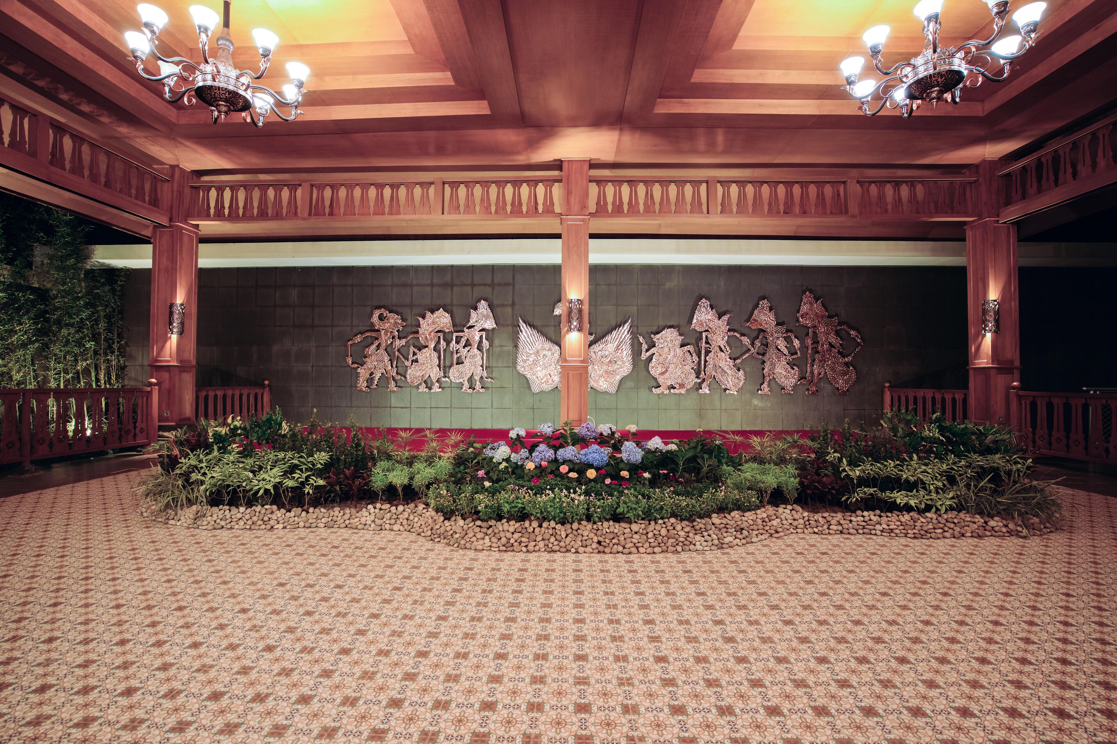Un salón amplio con vigas de madera ornamentadas, un suelo estampado y un arreglo floral central.