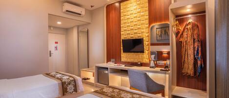 A hotel room with two beds, a desk with a flat-screen TV, a wardrobe, and a small seating area.