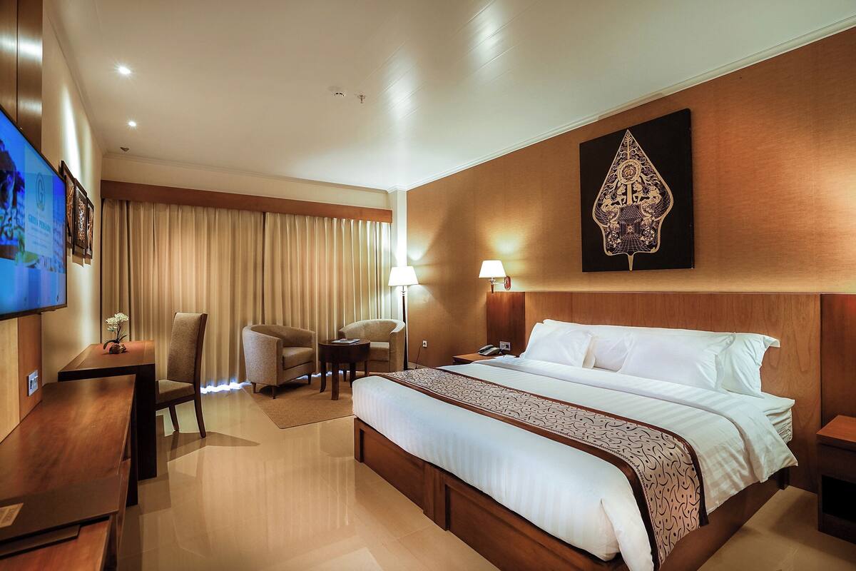 Habitación de hotel con una cama grande, un escritorio, una silla, un televisor y una obra de arte colgada en la pared.