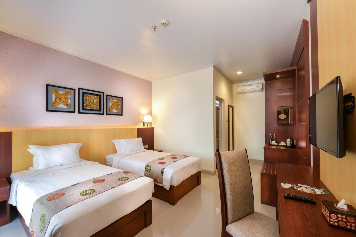 Habitación de hotel con dos camas, un escritorio, una silla, un televisor y obras de arte colgadas en la pared.
