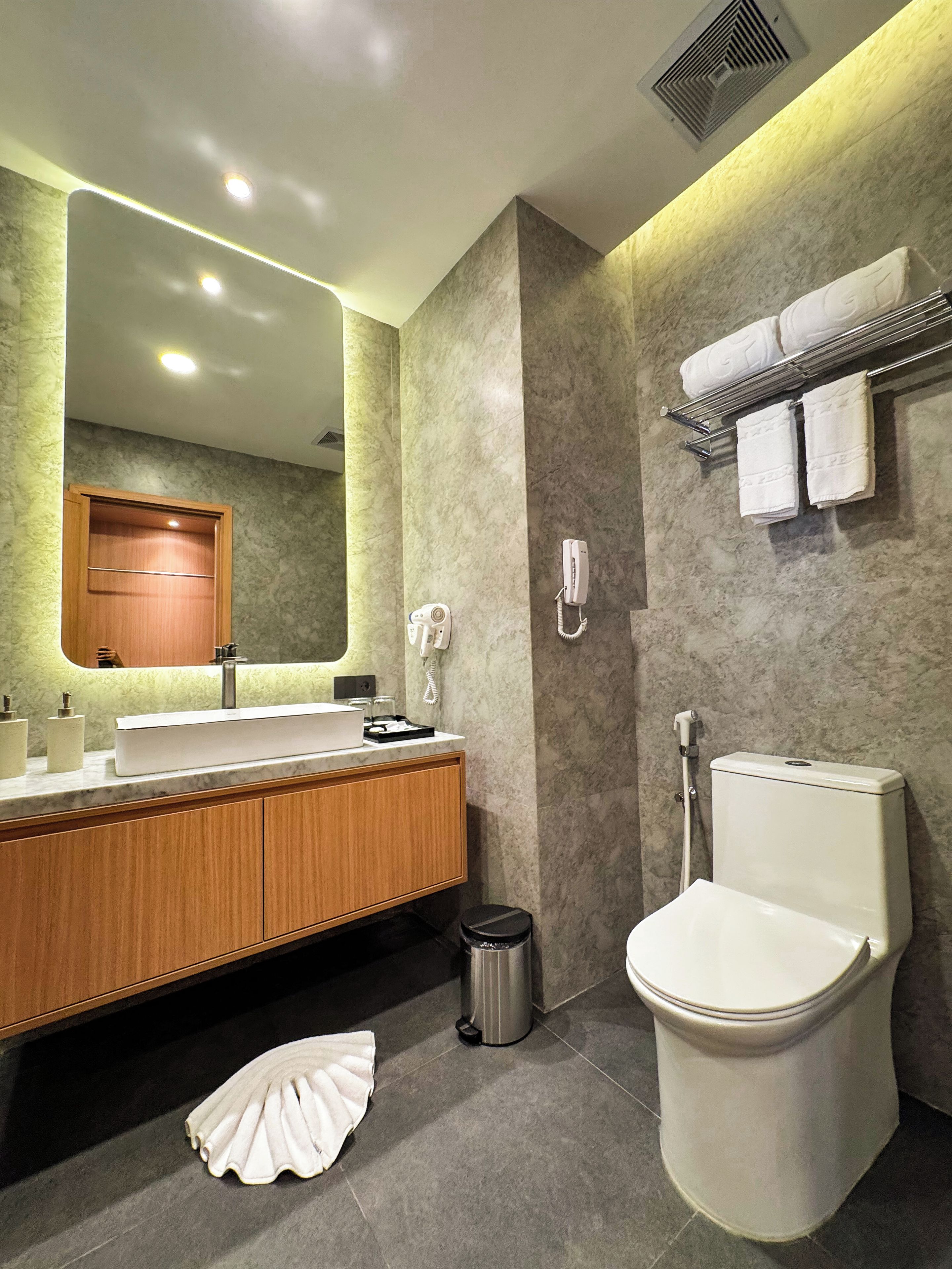 A modern bathroom with a marble sink, a toilet, a mirror, and a towel rack.