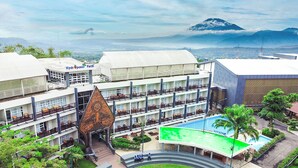 A hotel with multiple floors, a swimming pool, and a mountain in the background.