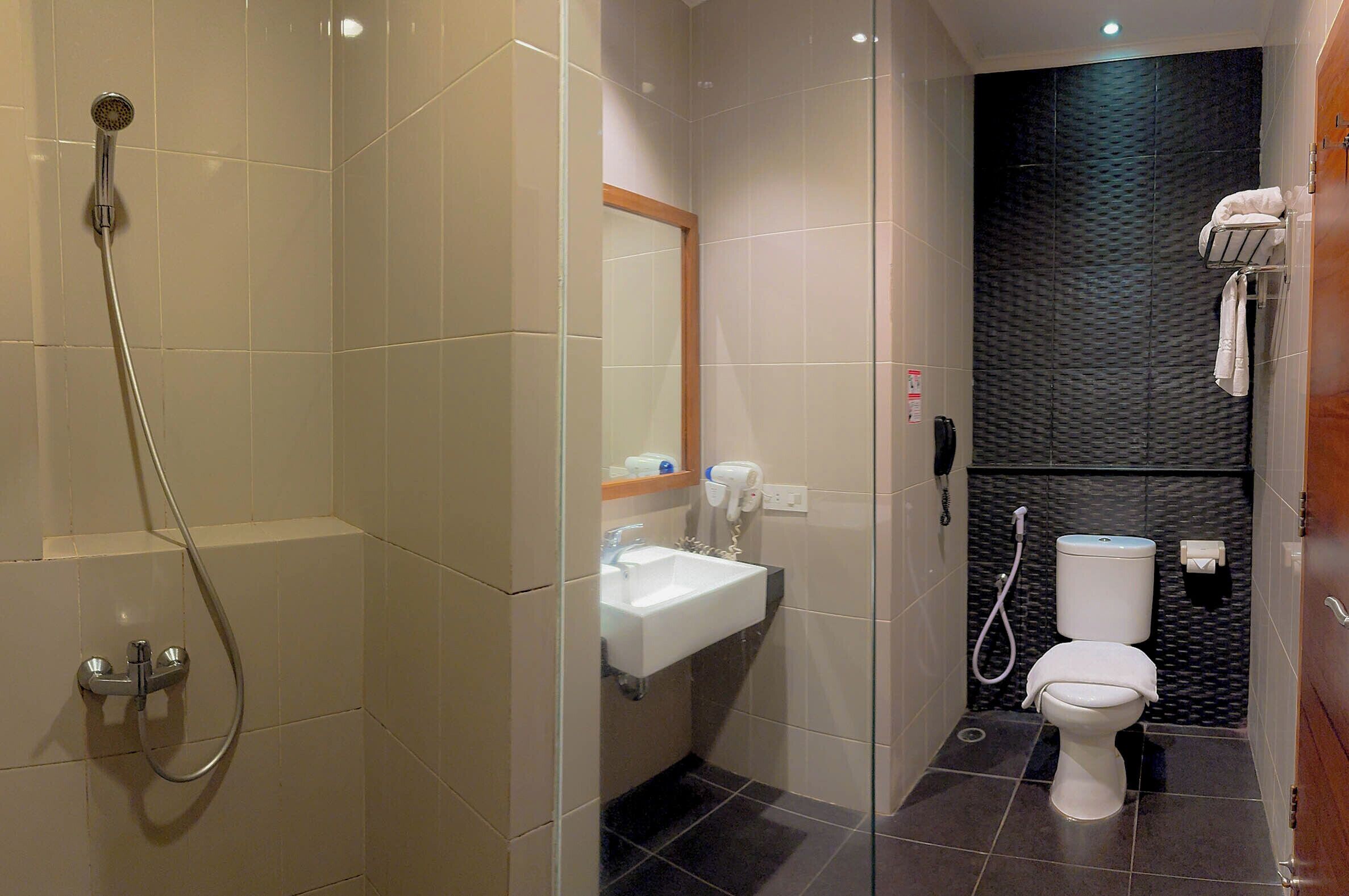 Baño pequeño con ducha, lavamanos e inodoro, que combina paredes con azulejos y una pared de acento texturizada oscura.