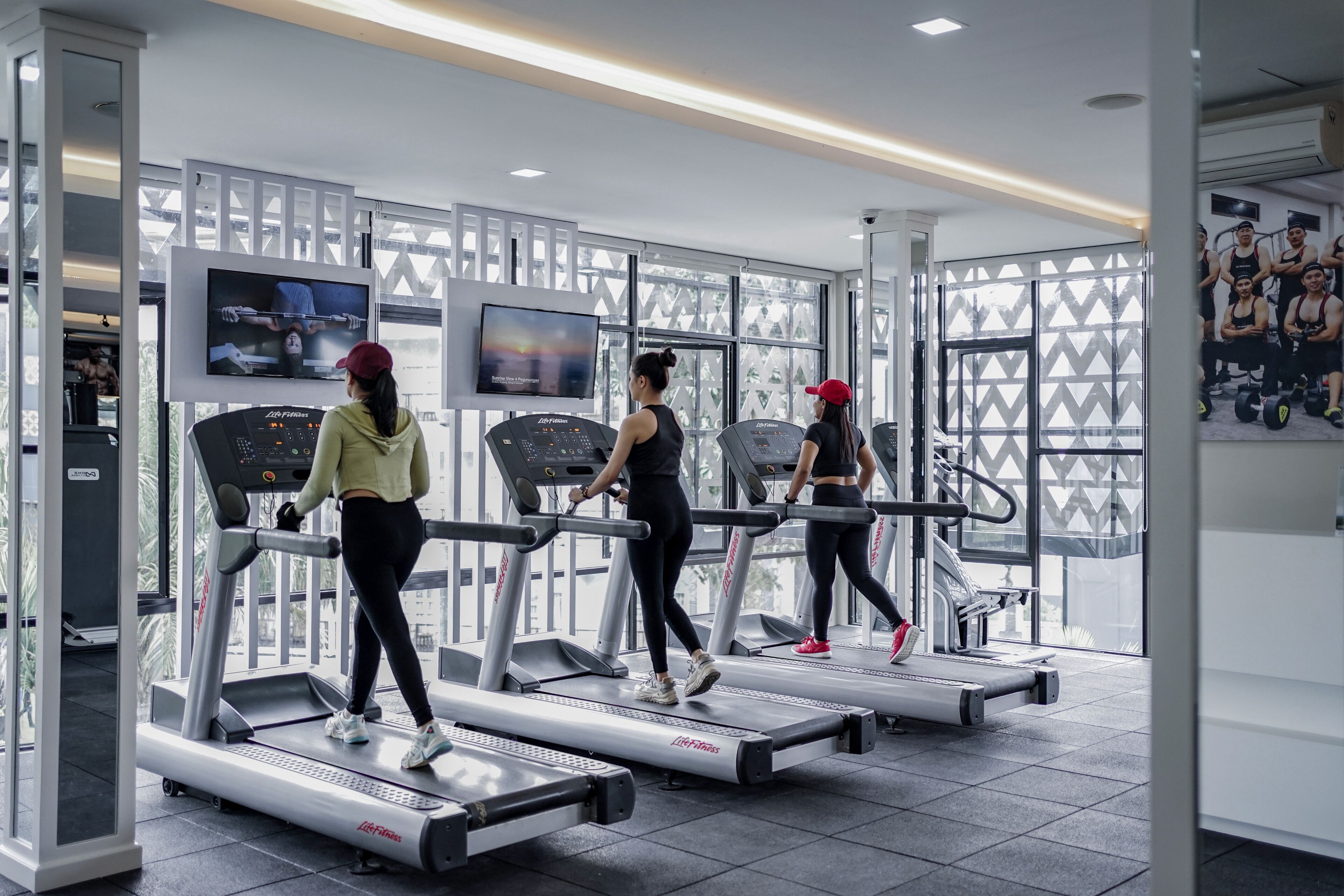 Ein Fitnessstudio mit Laufbändern, großen Fenstern und einem Fernsehbildschirm.