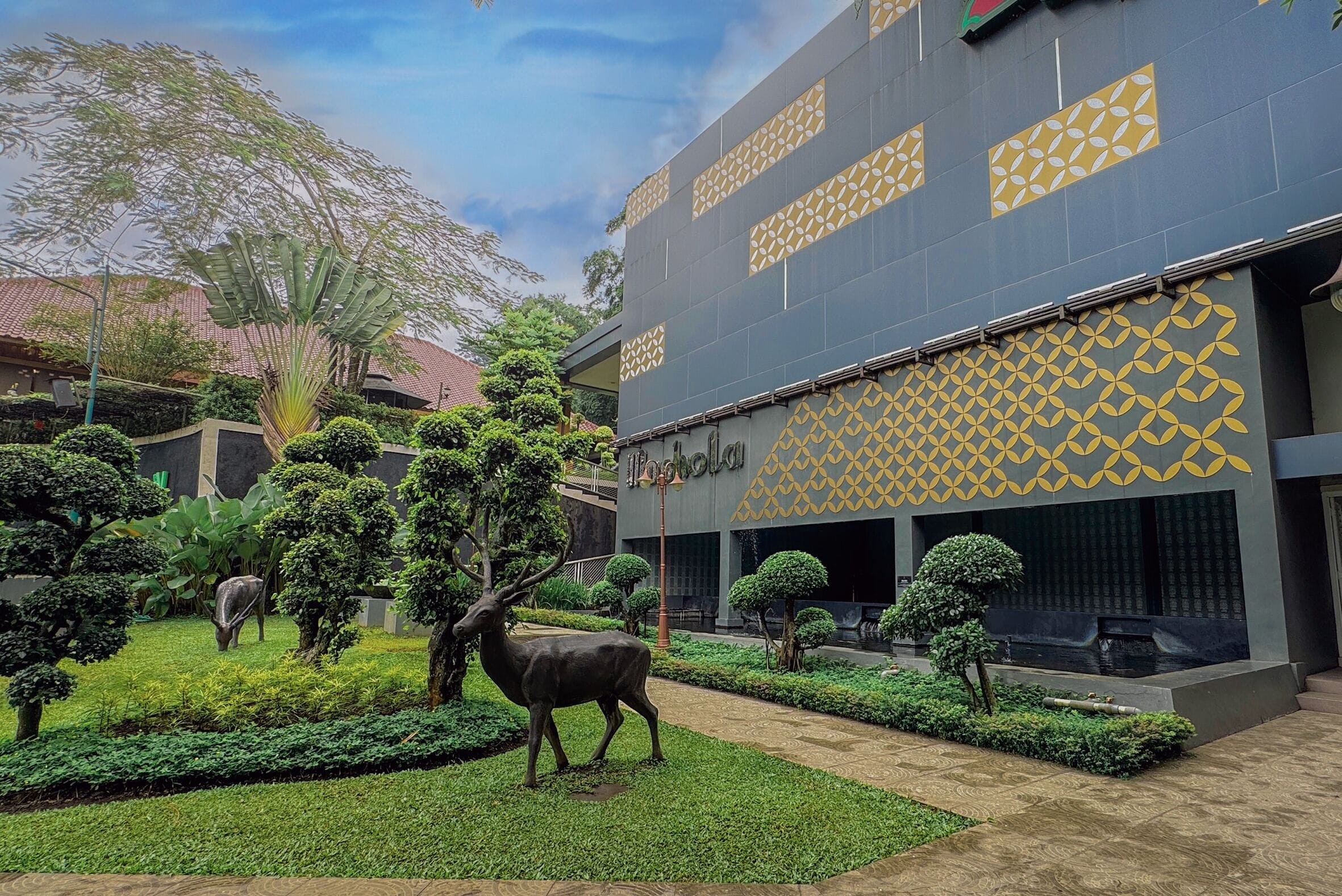A building with a patterned facade and a well-maintained garden with statues and trimmed hedges.