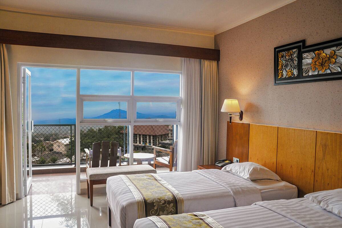 Habitación de hotel con dos camas, un balcón con mesa y sillas, y vistas a las montañas.