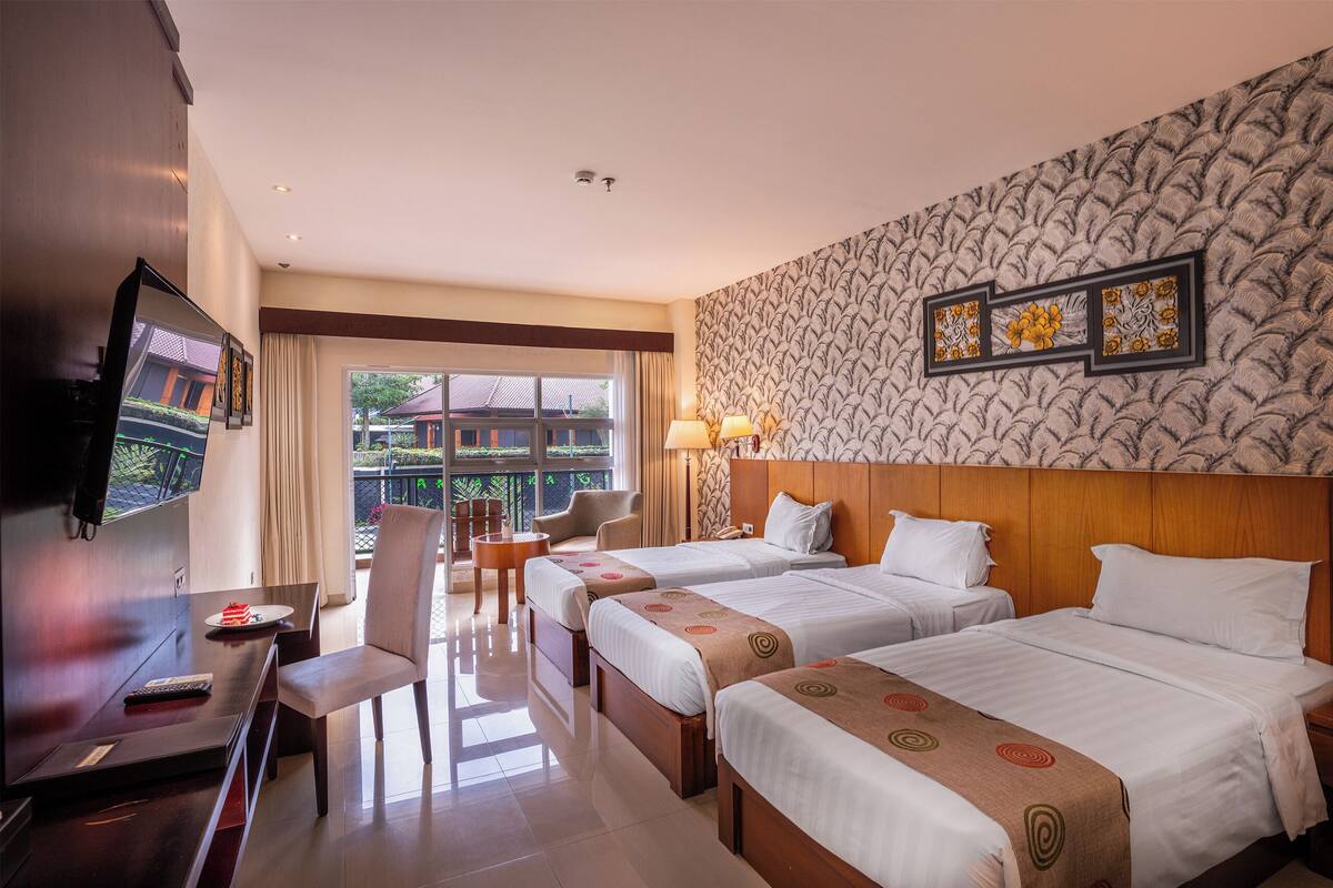 Habitación de hotel con tres camas, televisión, escritorio y balcón con vistas.