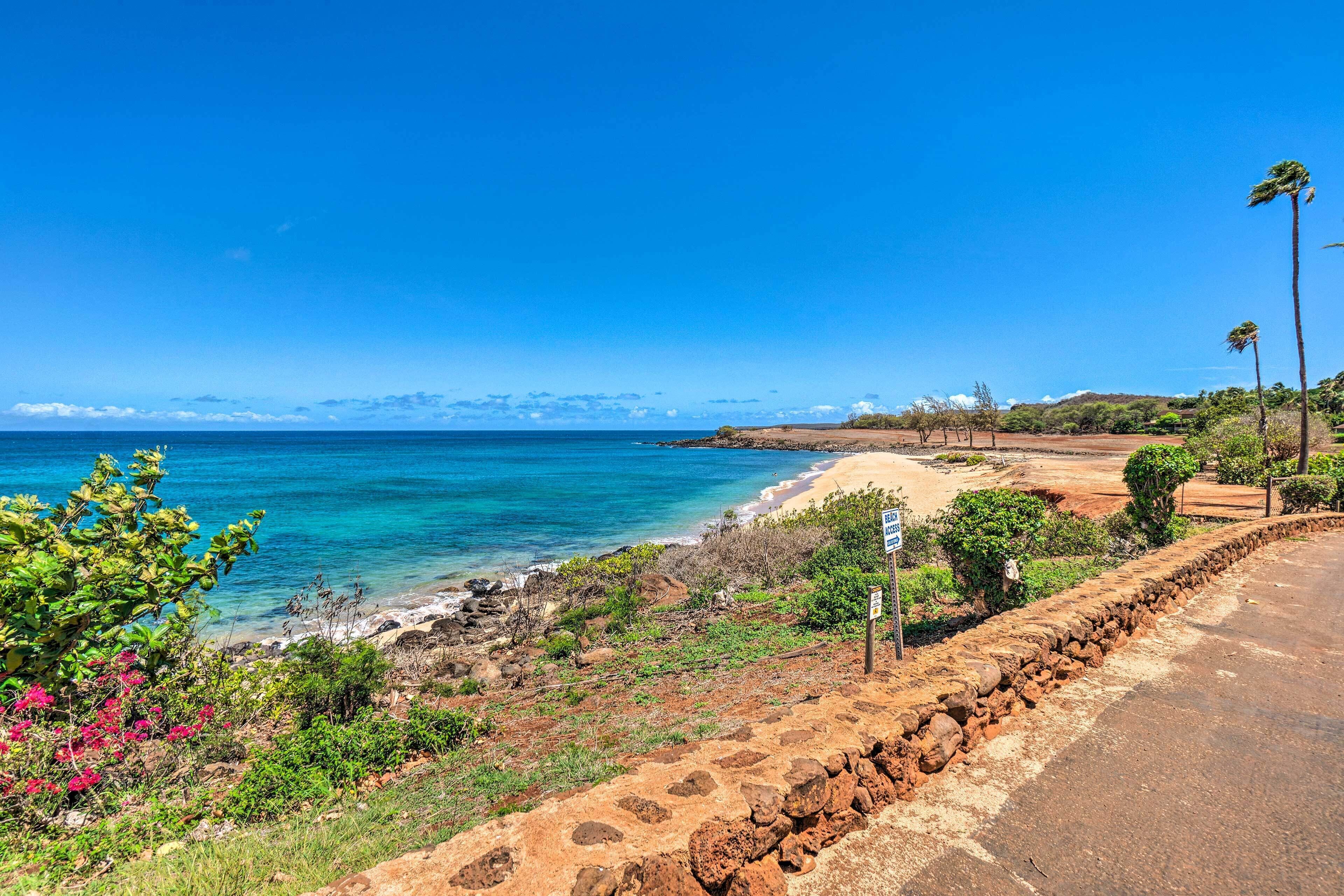 Une route côtière bordée d’un mur de pierres, avec une plage et un ciel bleu dégagé.