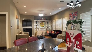 A modern kitchen with a large island, a dining area with red chairs, a sofa, and a red cart with a peace symbol.