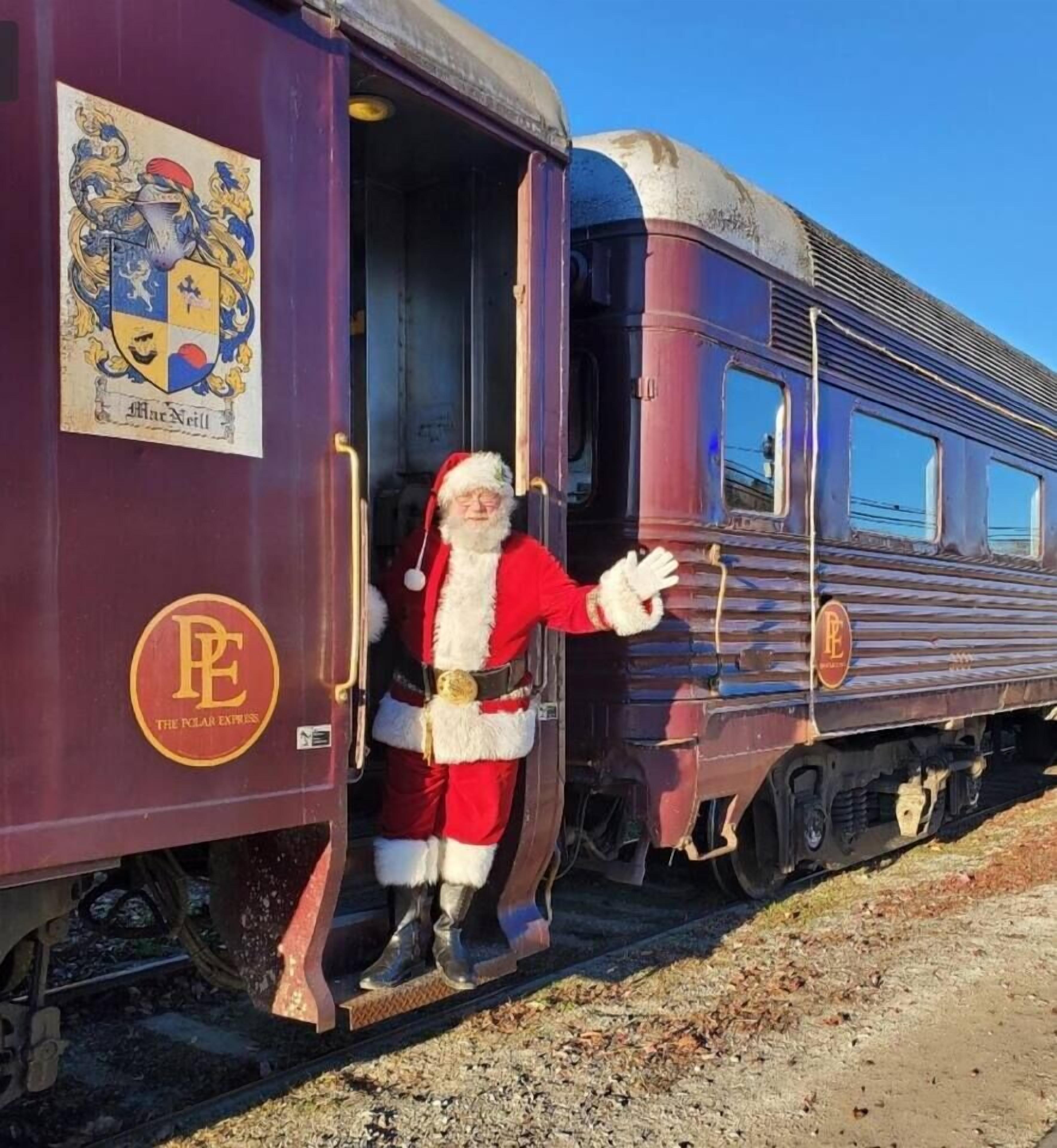 Un train avec une figurine du Père Noël debout à la porte ouverte, qui fait des signes de la main.