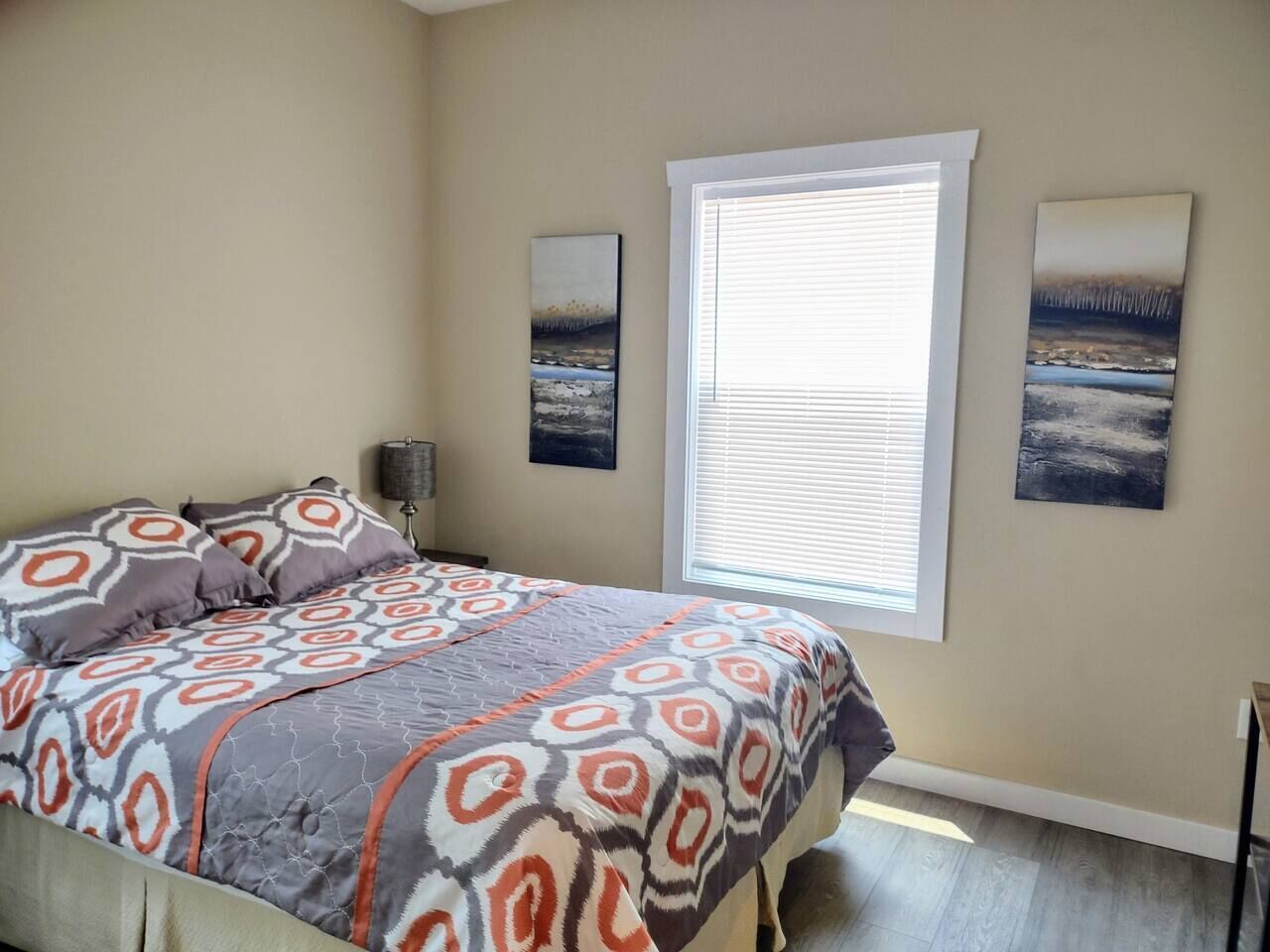 A bedroom with a bed, a window with blinds, and two wall-mounted paintings.