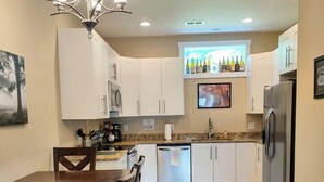 A modern kitchen with white cabinets, a stainless steel refrigerator, a dining table with chairs, and a chandelier. - Downtown Bryson City Flat - Walk to it All! (Bryson City)