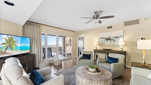 A spacious living room with a large flat-screen TV, comfortable seating, a ceiling fan, and a view to the outside. - "Bay Watch" - AWESOME Condo with a water view and golf cart! (Miramar Beach)