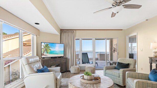 A spacious living room with a large TV, comfortable seating, a round coffee table, and a ceiling fan. - "Bay Watch" - AWESOME Condo with a water view and golf cart! (Miramar Beach)