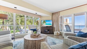 A spacious living room with large windows, a round coffee table, and comfortable seating. - "Bay Watch" - AWESOME Condo with a water view and golf cart! (Miramar Beach)