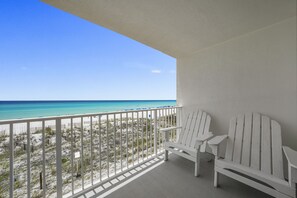 Un balcon avec deux fauteuils Adirondack blancs, une balustrade blanche et une vue sur une plage et l’océan.