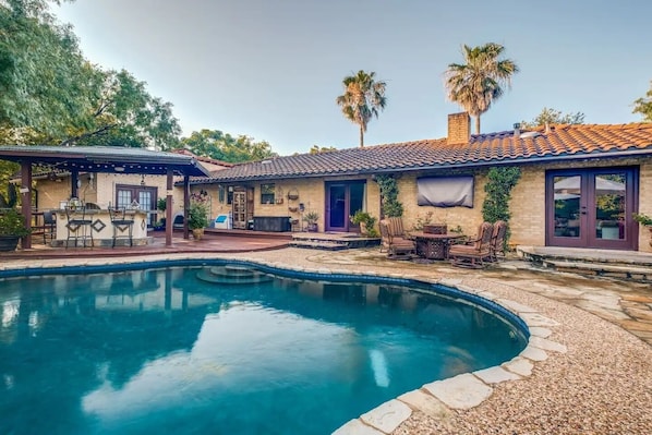 A pool area with a stone deck, outdoor furniture, and a house with a tiled roof and windows. - Mini Resort In SA, 3 Master Suites w Heated Pool, big screen & outdoor kitchen (San Antonio)
