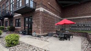 A brick building with a patio area featuring outdoor seating and a red umbrella.