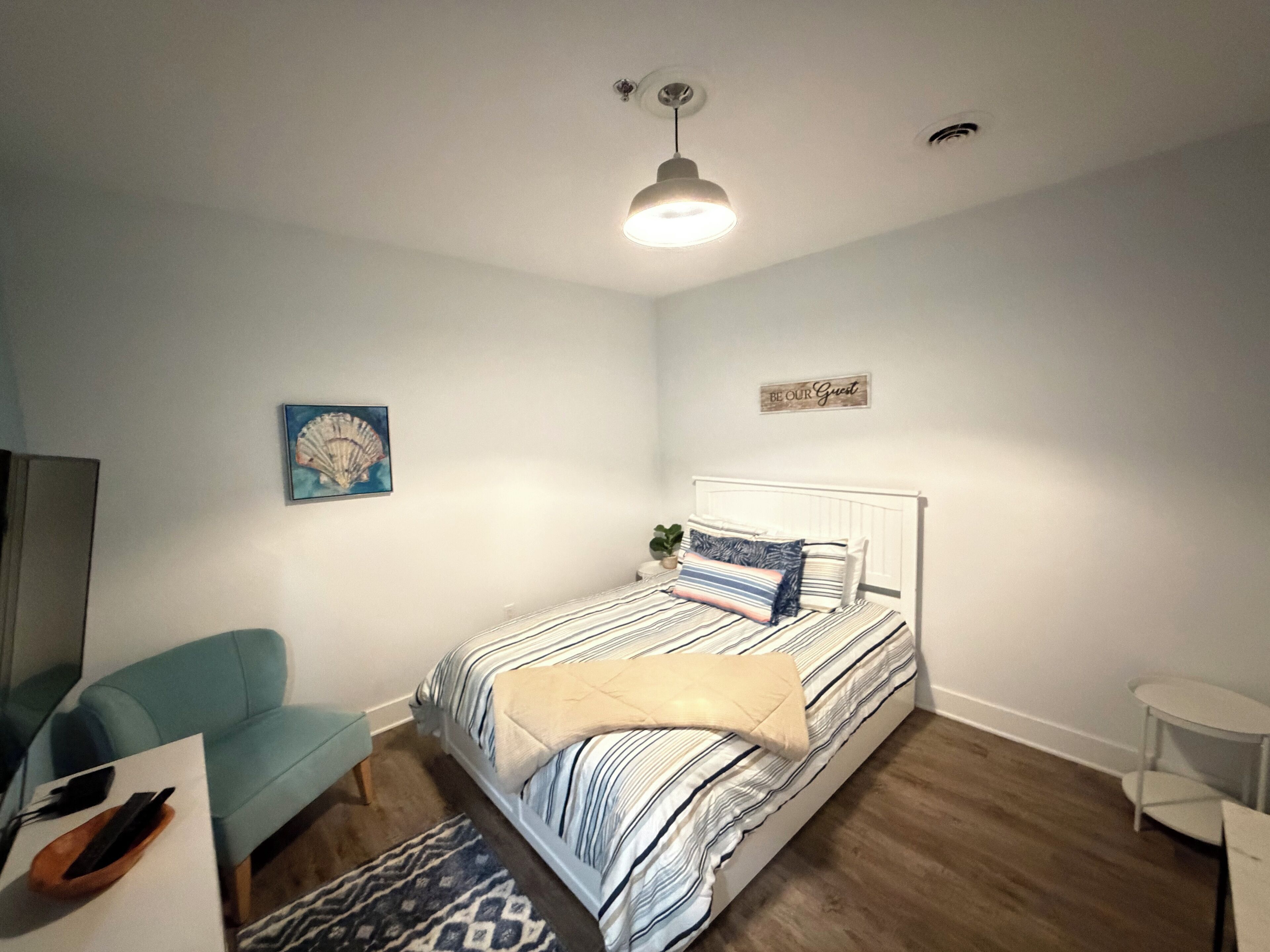 Une chambre à coucher avec un lit, une chaise bleue, une petite table et une étagère fixée au mur.