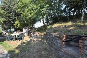 An outdoor patio with a stone wall, a brick barbecue grill, and a table with chairs.