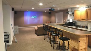 A conference room with a projector screen displaying "JVC," a long table with chairs, a kitchenette, and a whiteboard on the wall.