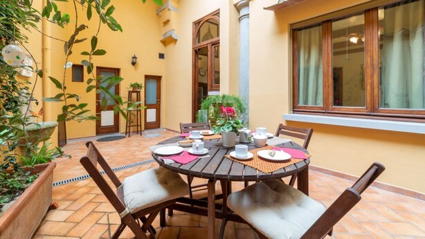 A round wooden table with chairs, a potted plant, and a window with curtains. - The paintress home with private patio (Firenze)