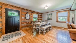 A dining area with a wooden table, chairs, and a bench. There is a black door with a window, a wall clock, and a ceiling light. - Sunny Daze by SoCharm | Hot Tub | Fire Pit | Dock | Great Views (Denver)